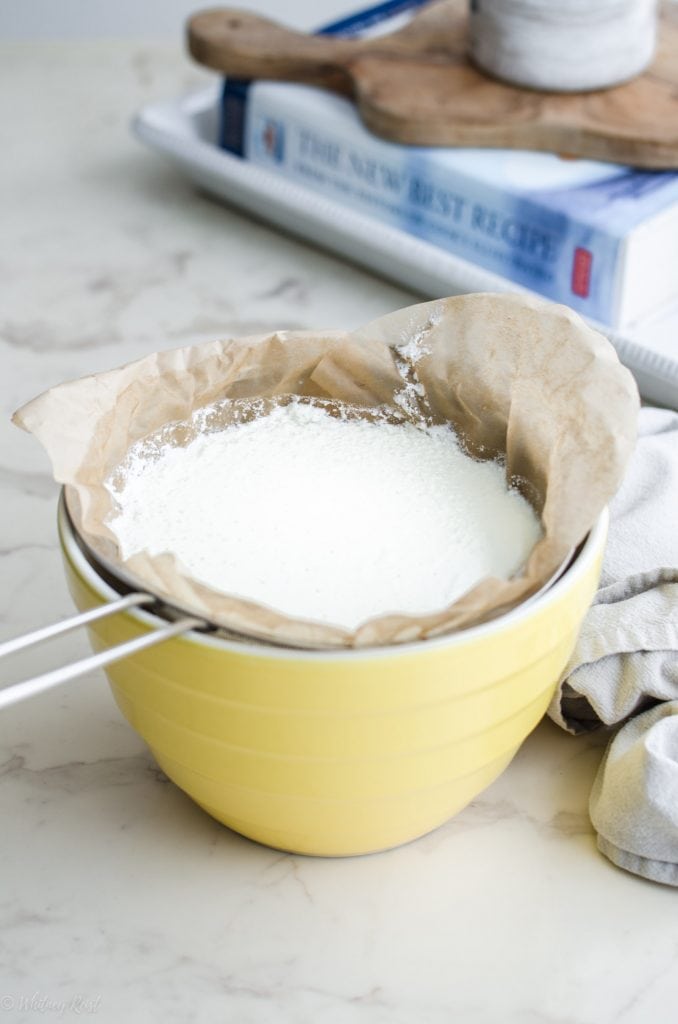 A yellow bowl with ricotta cheese being strained into it.