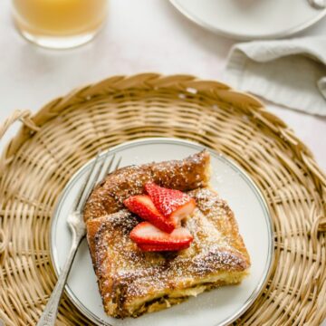 An overhead shot of a plate of ricotta French toast with strawberry syrup with a glass of orange juice on the side.