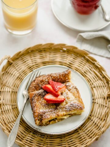 An overhead shot of a plate of ricotta French toast with strawberry syrup with a glass of orange juice on the side.