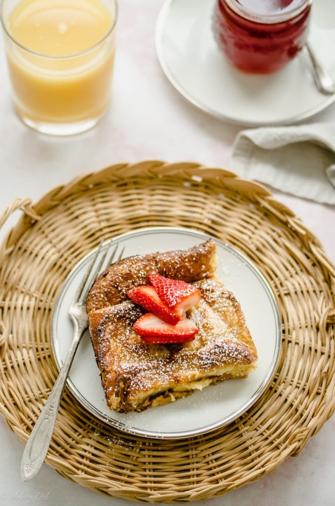 An overhead shot of a plate of ricotta French toast with strawberry syrup with a glass of orange juice on the side.