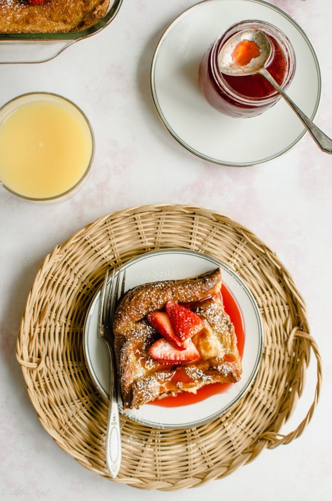 An overhead shot of a plate of ricotta French toast with strawberry syrup with a glass of orange juice on the side.