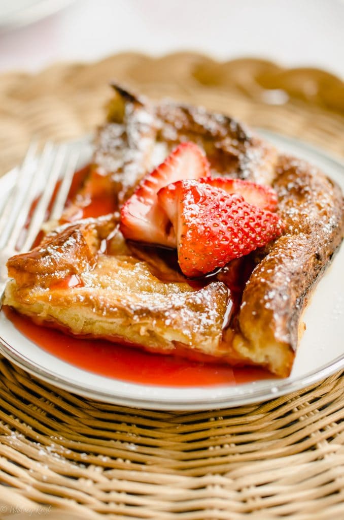 A close-up shot of a slice of French toast with strawberry syrup and strawberries on top.