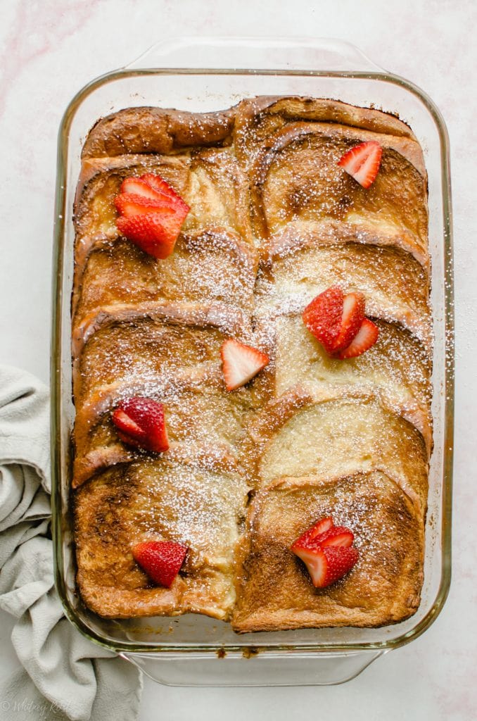 A glass casserole dish of overnight ricotta French toast with strawberries on top.