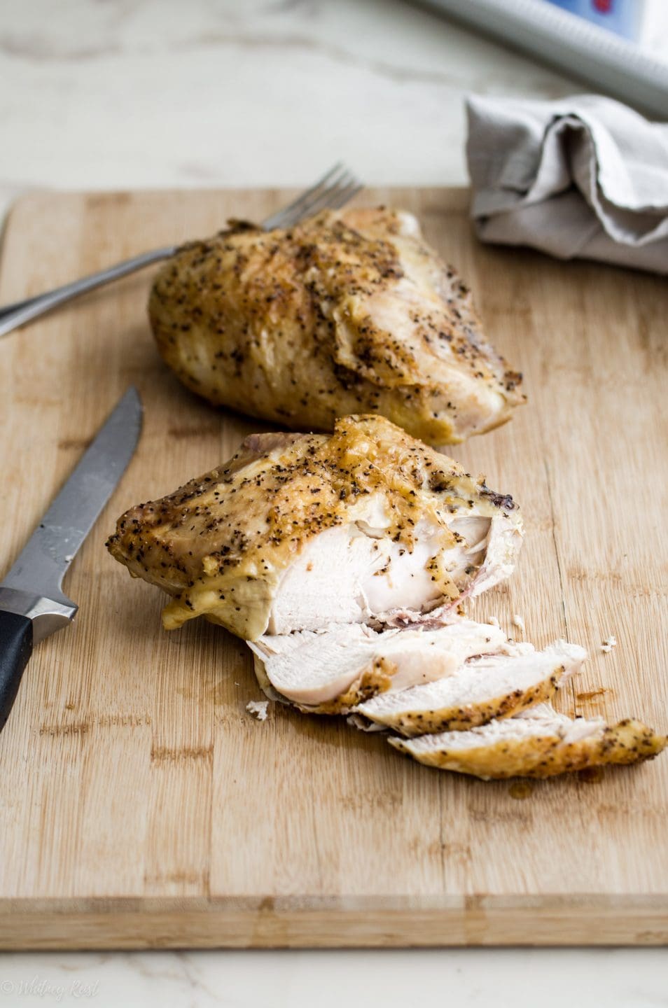 A roasted chicken breast being sliced on a cutting board on a white marble counter top.
