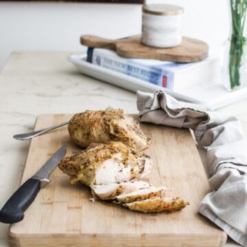 A roasted chicken breast being sliced on a cutting board on a white marble counter top.