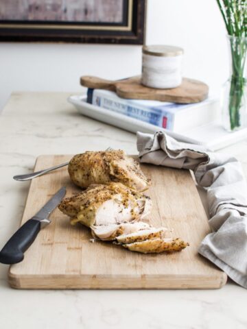 A roasted chicken breast being sliced on a cutting board on a white marble counter top.