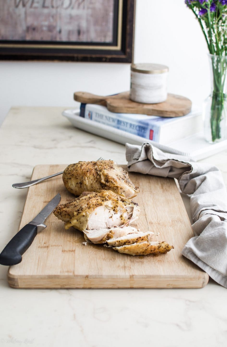 A roasted chicken breast being sliced on a cutting board on a white marble counter top. 