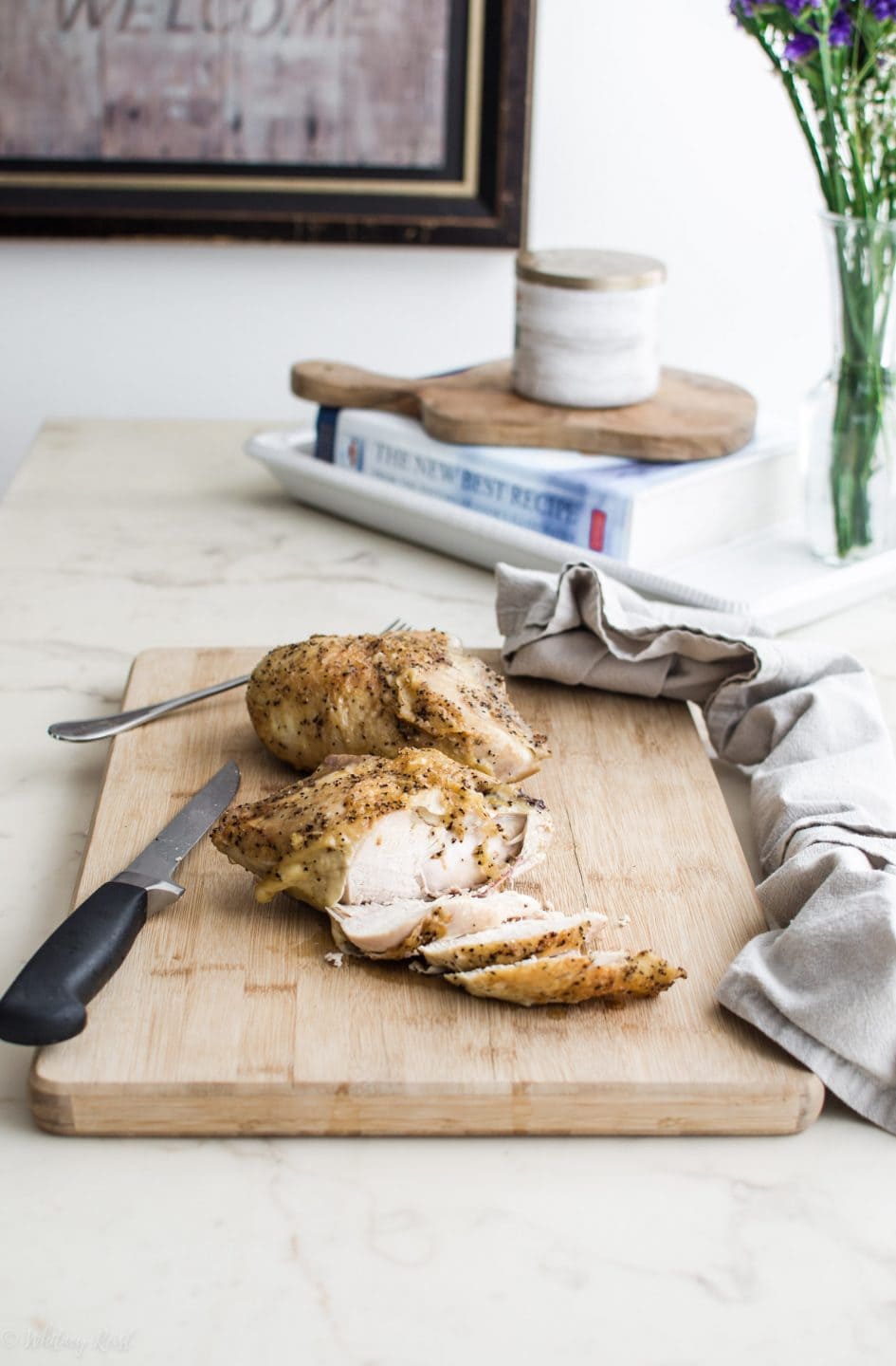 A roasted chicken breast being sliced on a cutting board on a white marble counter top.