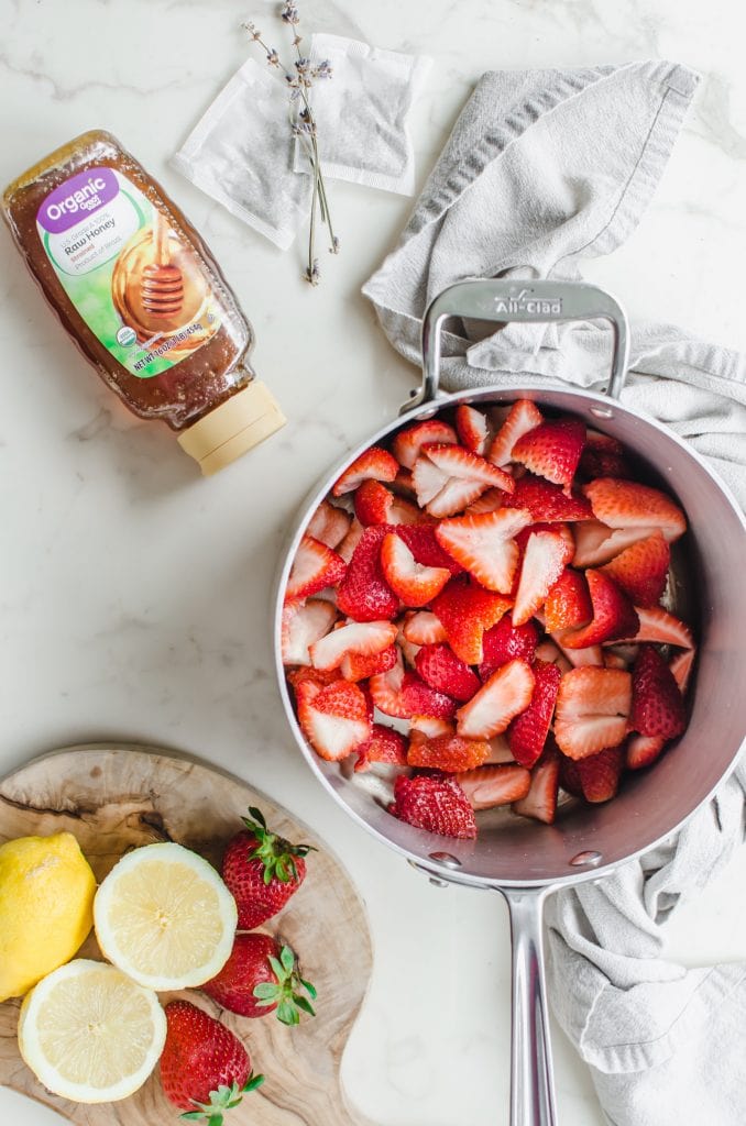 A pot with chopped strawberries and a bottle of honey. 