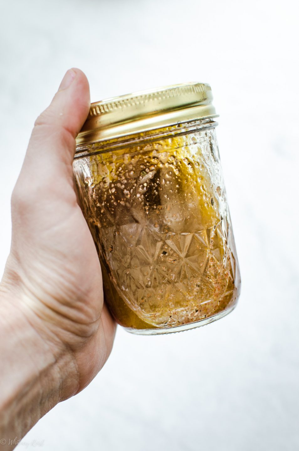 A hand holding a mason jar to shake up the contents of an Italian vinaigrette.