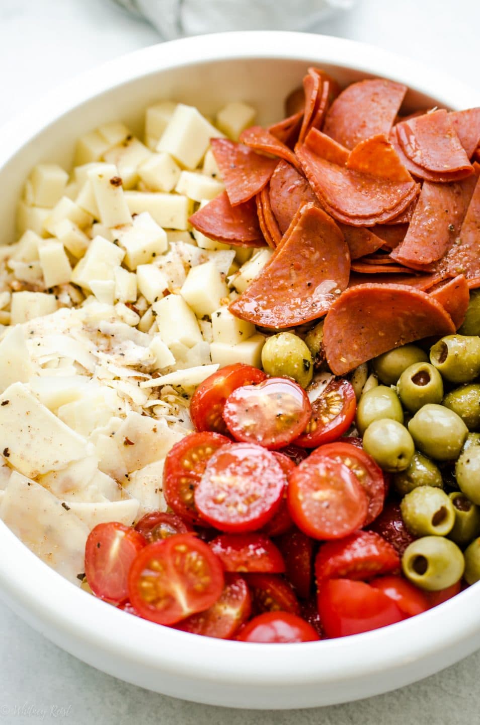 A white bowl filled with ingredients for Pizza Pasta Salad before the salad is tossed.