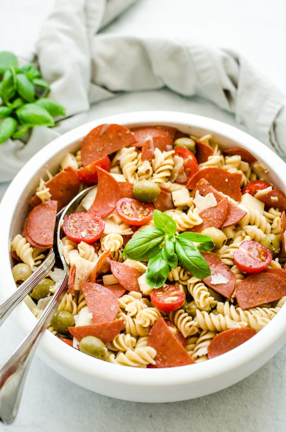 A white bowl filled with pizza pasta salad garnished with fresh basil leaves.