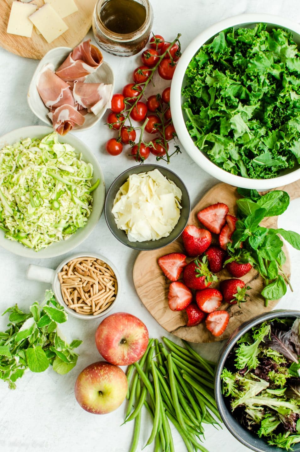 A flat lay of fruits and vegetables for a salad bar on a white marble surface.