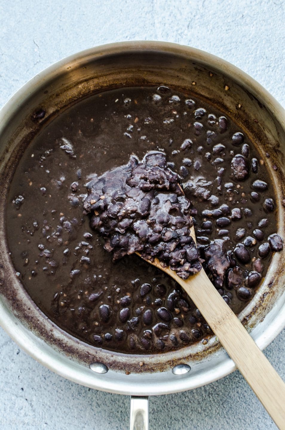 A skillet with partially mashed black beans and a wooden spoon.