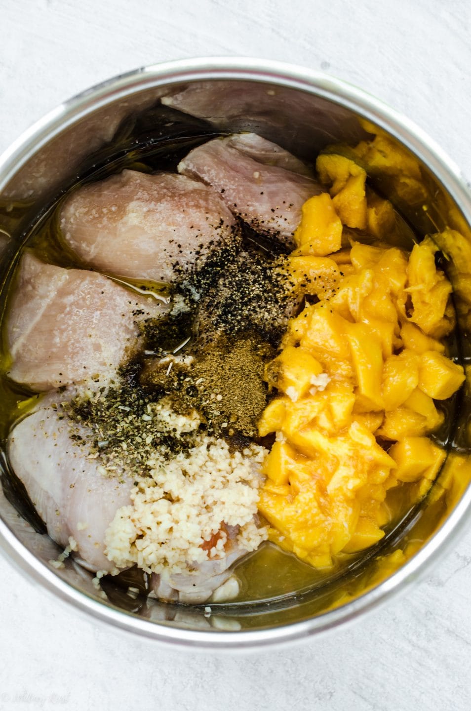 An overhead shot of the inside of an Instant Pot with uncooked chicken breasts, diced mangoes, garlic, and spices.