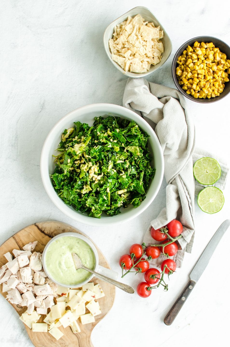 Bowls of ingredients for chopped Mexican kale salad on a white counter top.