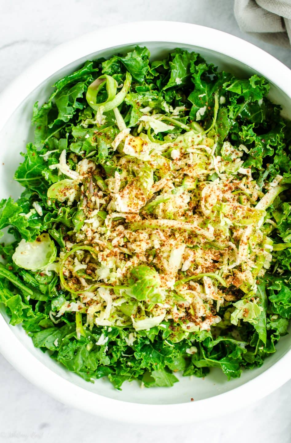 Chopped kale and shaved brussels sprouts in a white bowl.