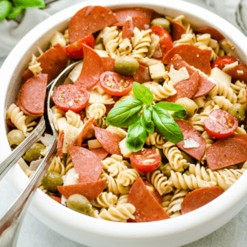 A white bowl filled with pizza pasta salad garnished with fresh basil leaves.