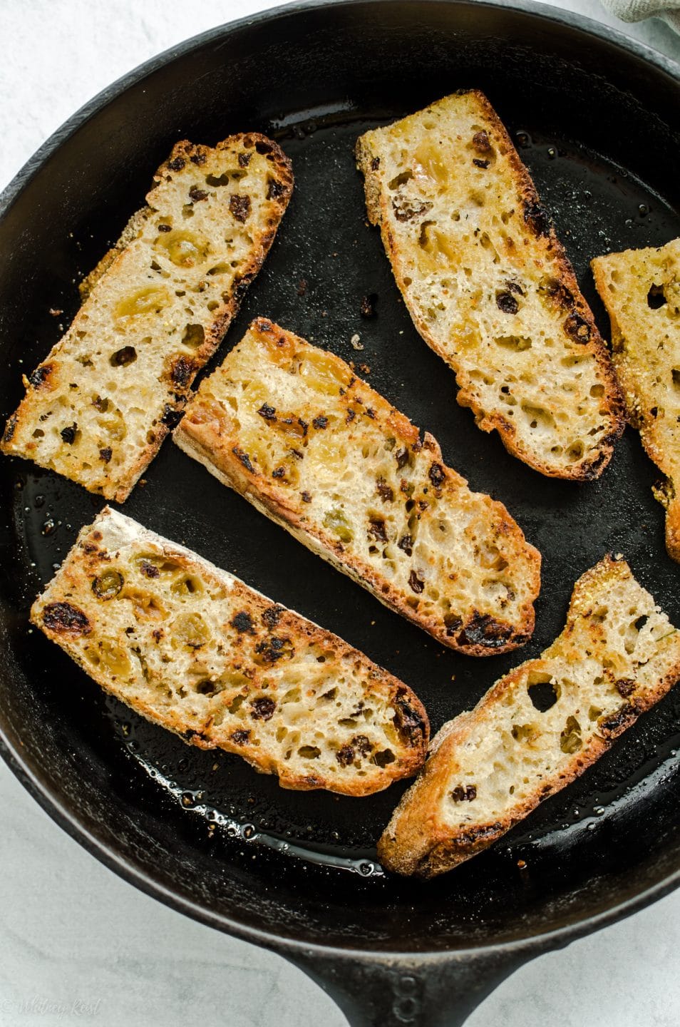 A cast iron skillet with pieces of rosemary raisin toast.