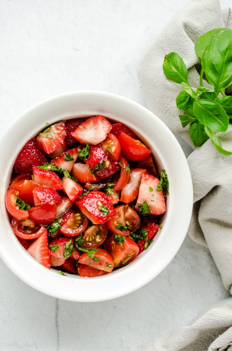 A white bowl with chopped tomatoes and strawberries with basil.