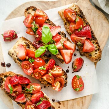 An overhead shot of strawberry bruschetta on parchment paper and a cutting board.