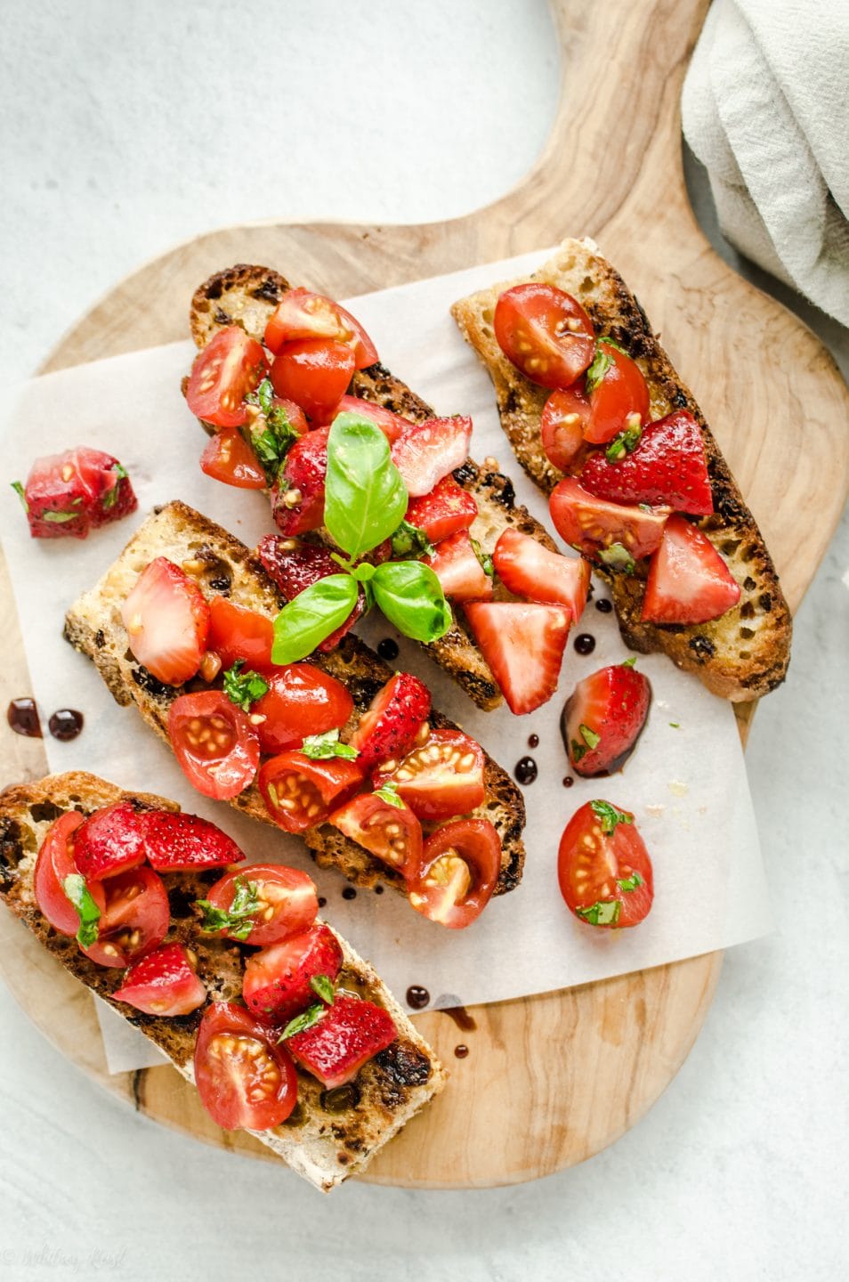 An overhead shot of strawberry bruschetta on parchment paper and a cutting board.