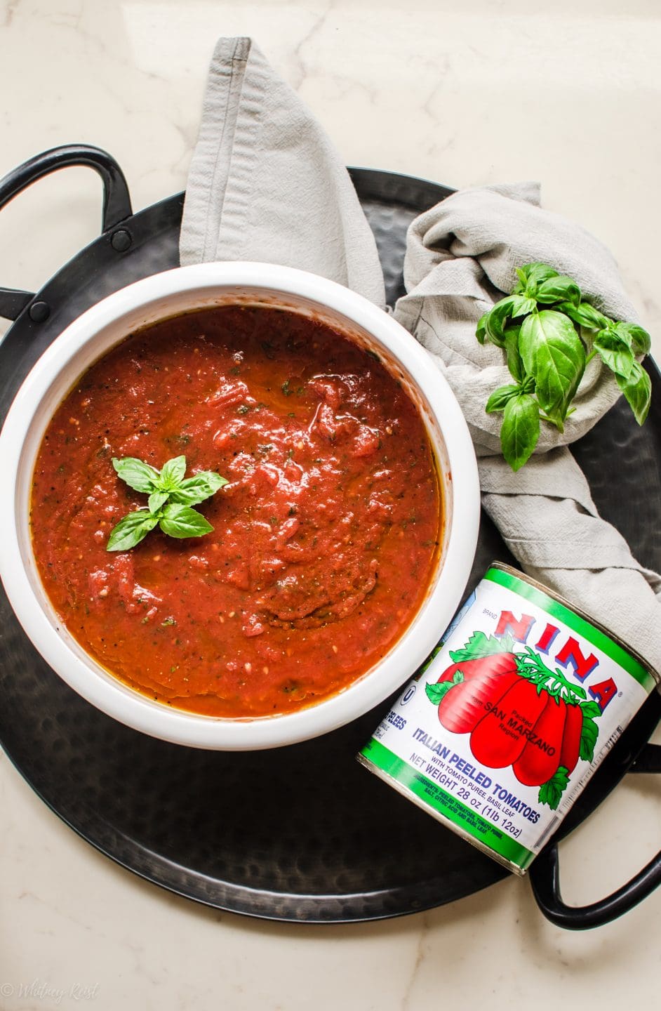 An overhead shot of a white bowl with tomato pizza sauce and can of San Marzano tomatoes on the side. 