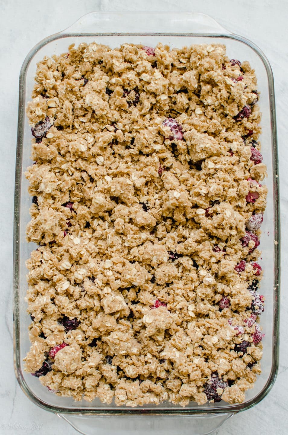 An unbaked mixed berry crumble in a glass baking dish.