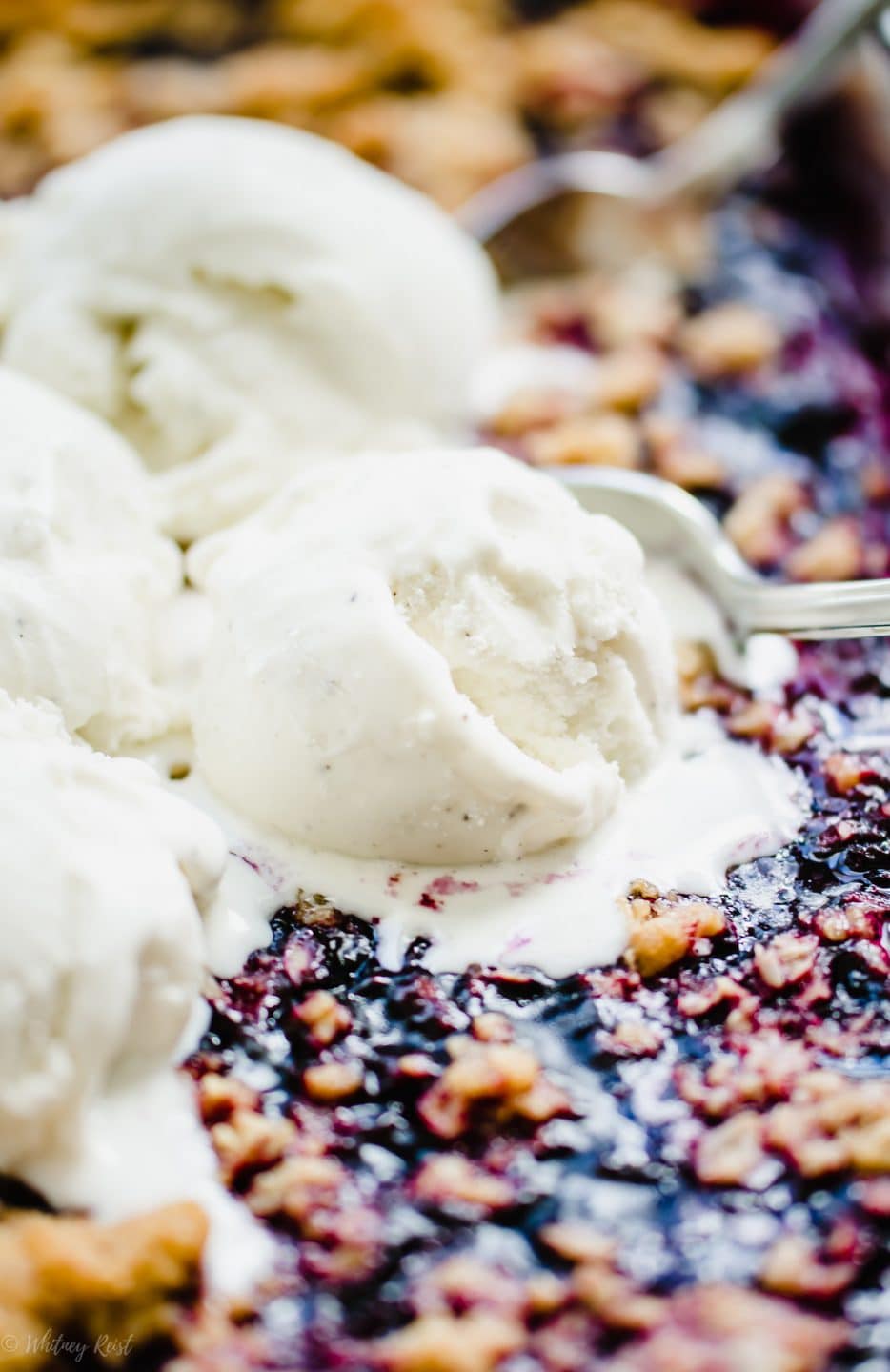 A scoop of ice cream melting on top of a dish of mixed berry crumble.