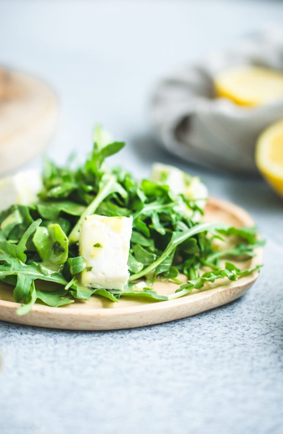 A close up side shot of a wooden plate with arugula feta salad. 