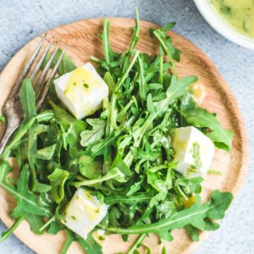 A close up overhead shot of a plate with arugula salad and a white bowl with mint dressing on the side.