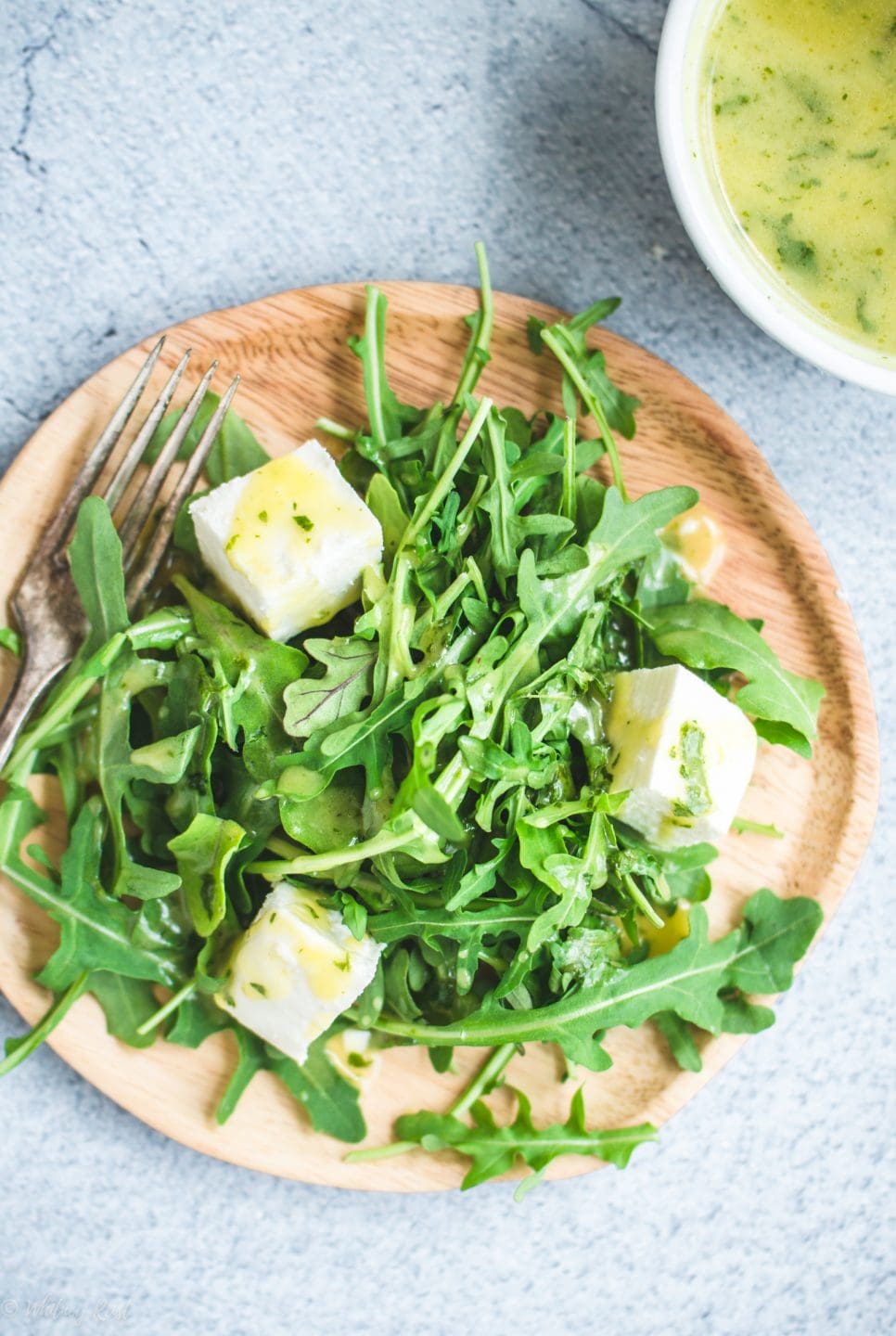 A close up overhead shot of a plate with arugula salad and a white bowl with mint dressing on the side. 