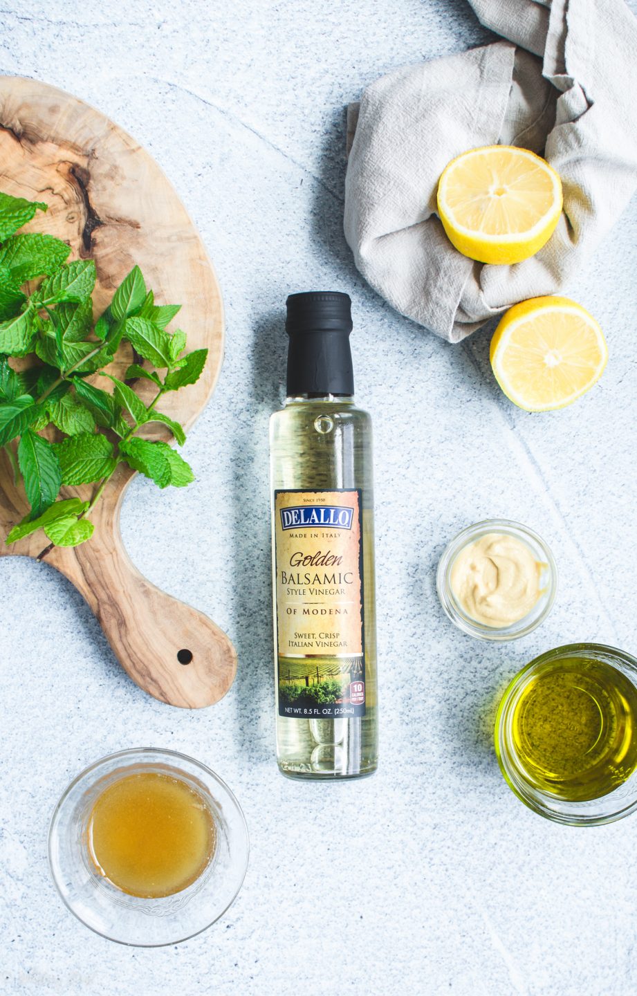 A bottle of Delallo white balsamic vinegar with measured ingredients for making a vinaigrette in bowls on the side.  