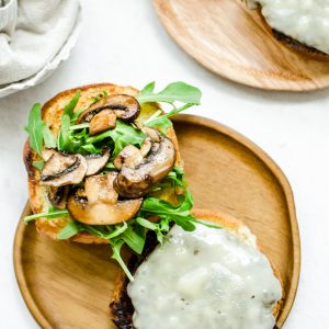 An overhead shot of an open faced mushroom swiss smashburger on a wooden plate.