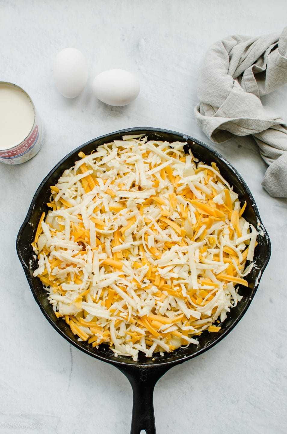 An cast iron skillet of unbaked mac and cheese with a can of evaporated milk and eggs on the side.