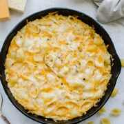An overhead shot of a cast iron skillet of baked mac and cheese with dried pasta and cubes of cheese around it.