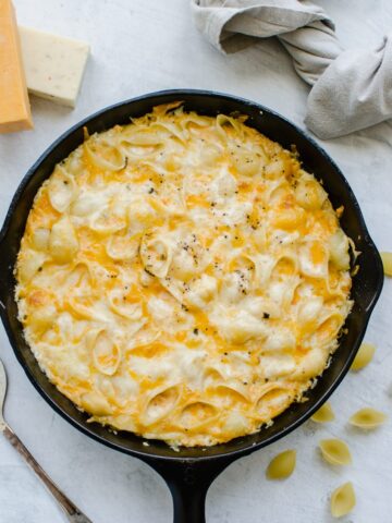 An overhead shot of a cast iron skillet of baked mac and cheese with dried pasta and cubes of cheese around it.