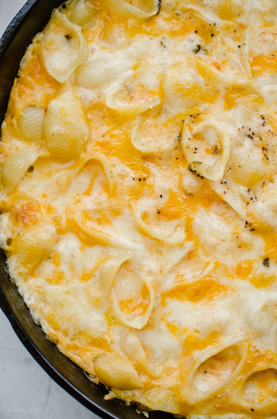 A close up shot to show the texture of a baked mac and cheese in a cast iron skillet.