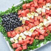 A white platter with a red, white, and blue watermelon flag salad on top on a blue stone background.