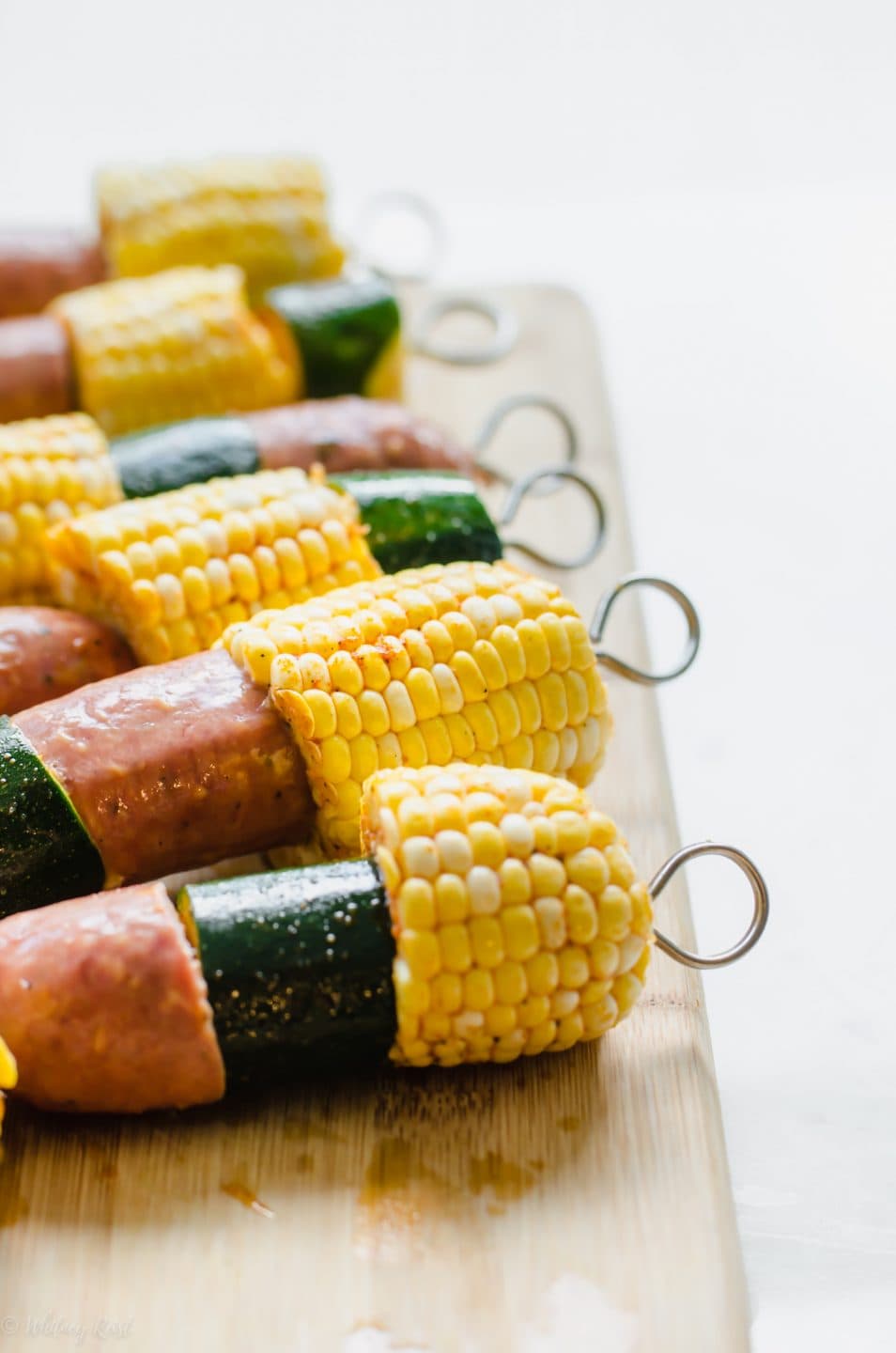 Grilled sausage, corn, and zucchini kabobs on a bamboo cutting board.