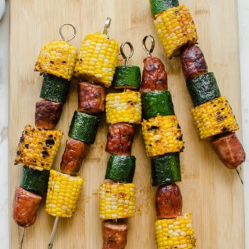 Grilled sausage, corn, and zucchini kabobs on a bamboo cutting board.