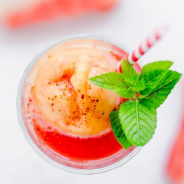 An overhead shot of the top of a glass filled with watermelon juice and mango sorbet with a red striped straw and sprig of mint.