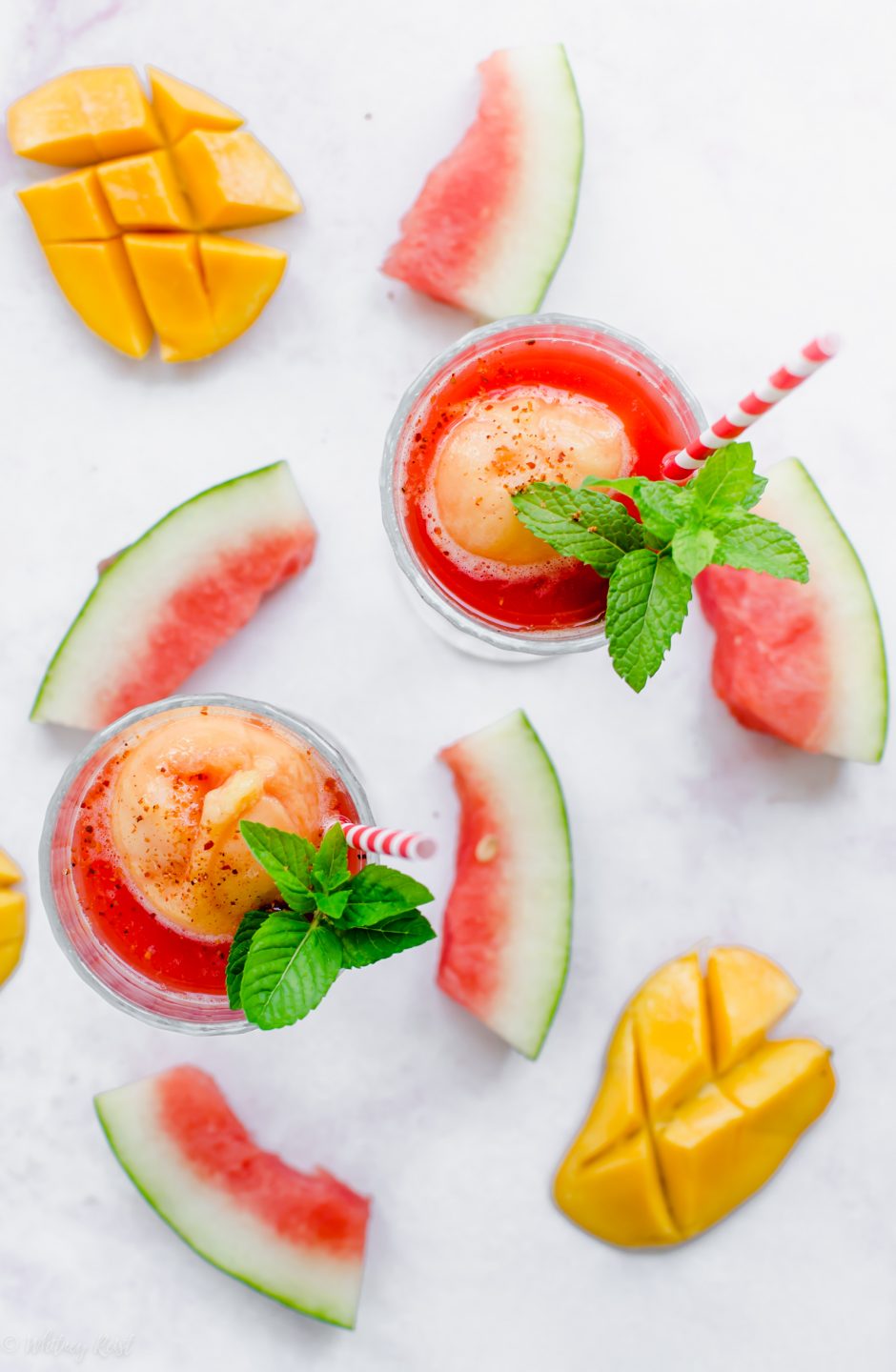 An overhead shot of two glasses of watermelon mango floats with slices of watermelon and mango surrounding the glasses.