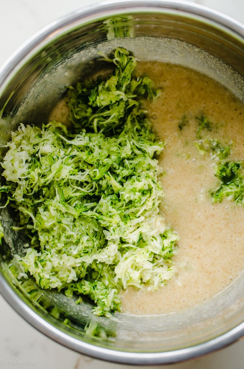 A mixing bowl with coffee cake batter and grated zucchini on the side.