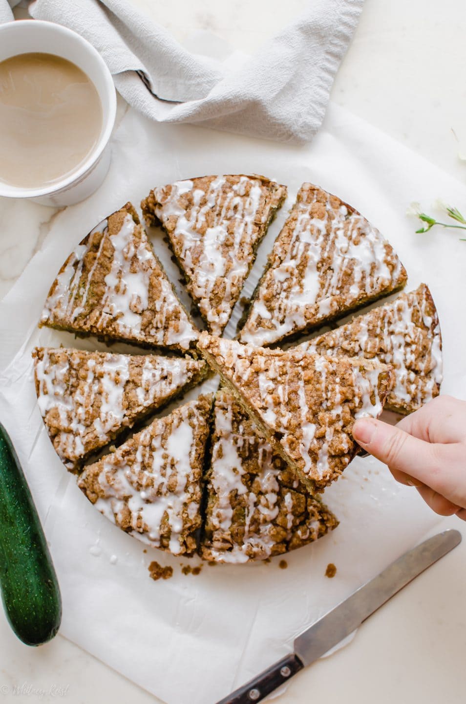 An overhead shot of a sliced zucchini coffee cake with a hand lifting a slice from the center.