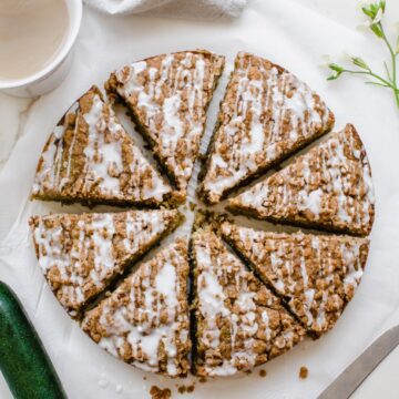 An overhead shot of a sliced zucchini coffee cake with a cup of coffee on the side.