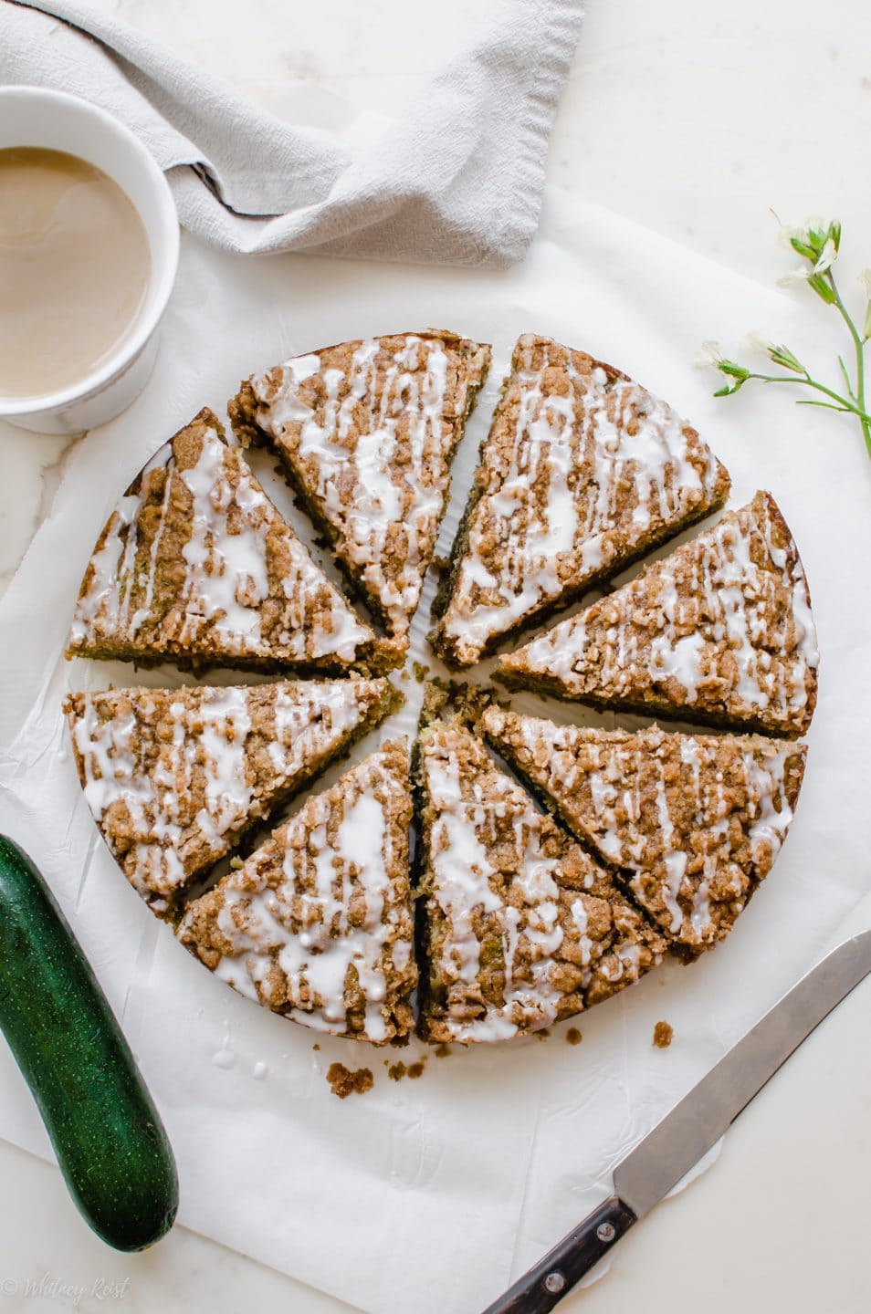 An overhead shot of a sliced zucchini coffee cake with a cup of coffee on the side.