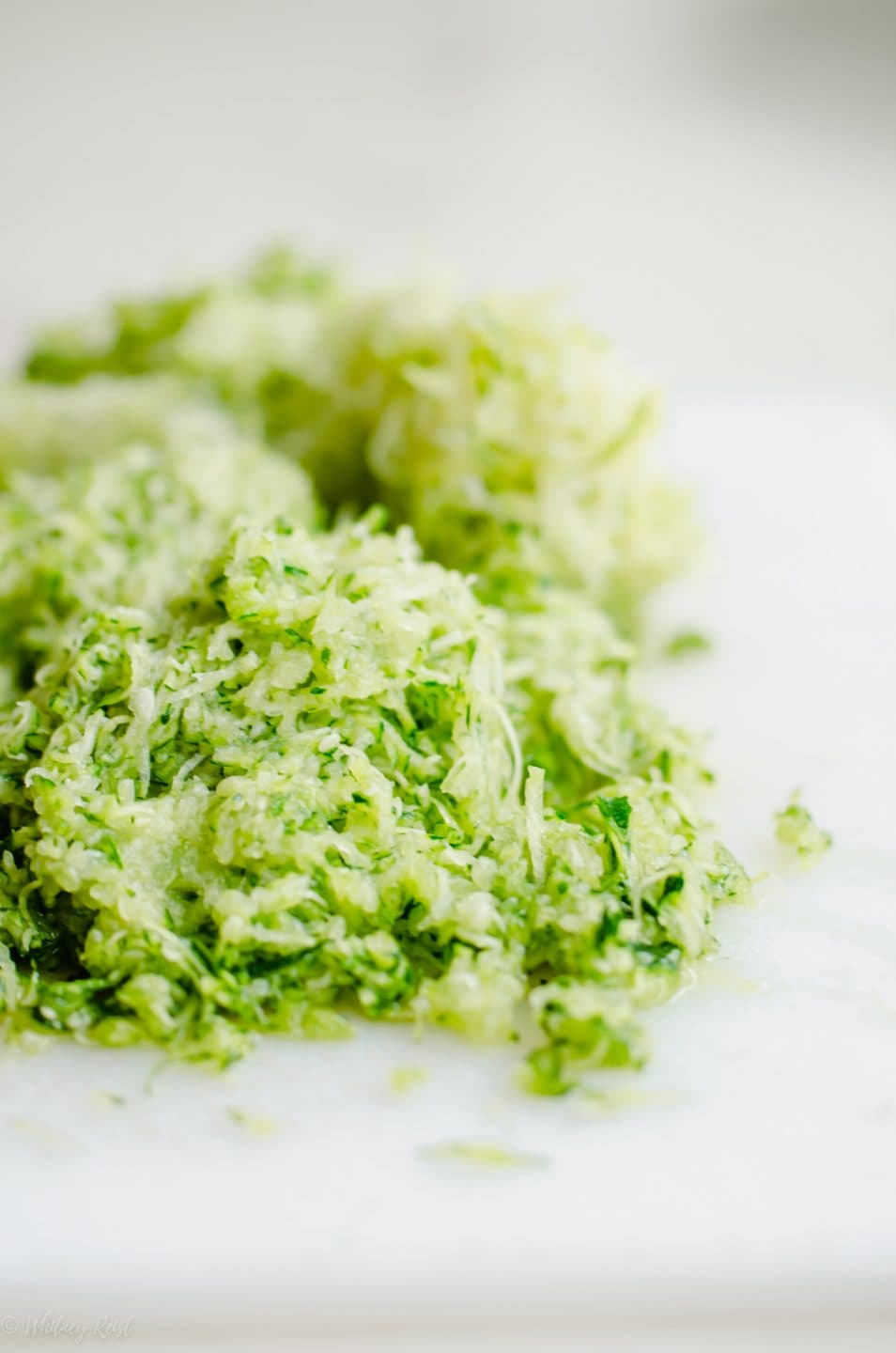 A pile of finely grated zucchini on a white cutting board.