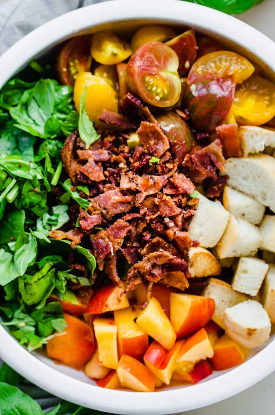 An overhead shot of the ingredients for BLT panzanella salad in a white bowl. 