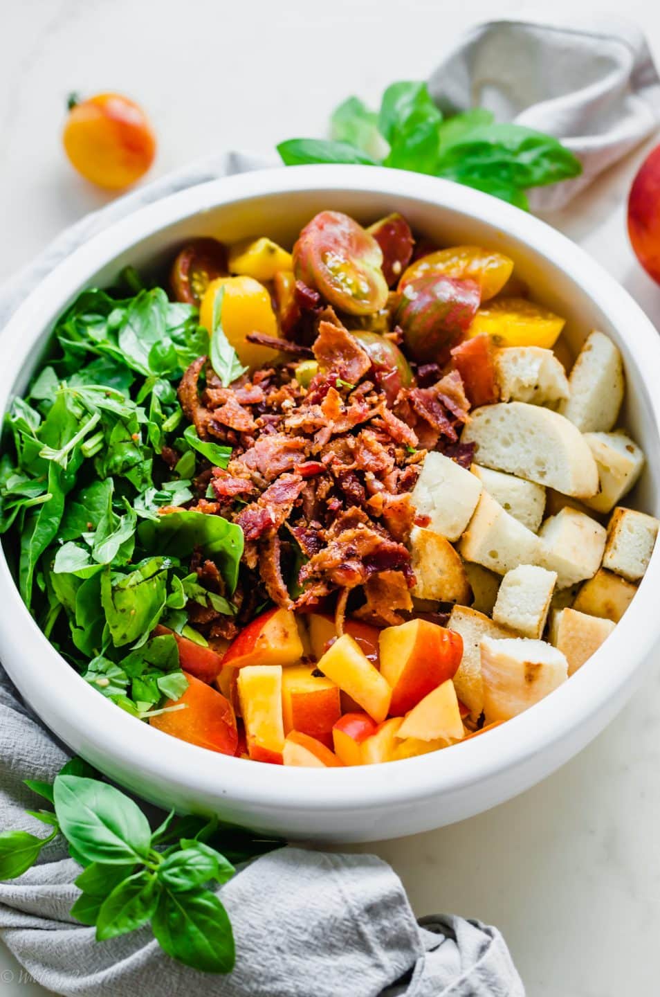 A close, overhead photo of the ingredients for BLT Panzanella Salad in a serving bowl before being mixed together.